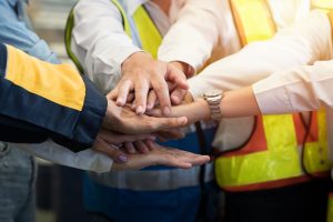 Group of male and female factory workers standing putting their hands together in industry factory. Factory workers stack of hands in factory. Unity and teamwork concept